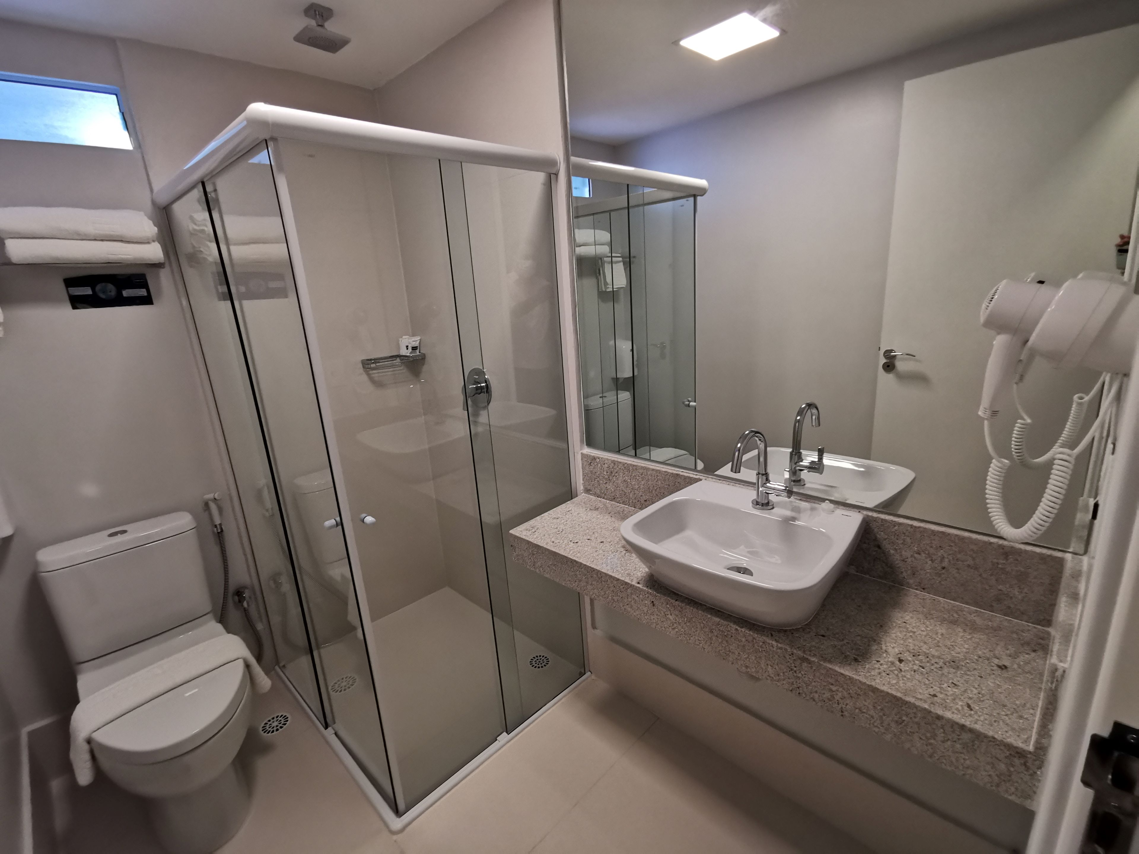 A modern bathroom with a glass-enclosed shower, a toilet, a sink with a mirror, and a hairdryer.