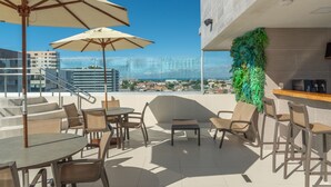 A rooftop terrace with outdoor seating, a bar area, and a view of the cityscape. - Verano Pajuçara by Tropicalis (Maceió)