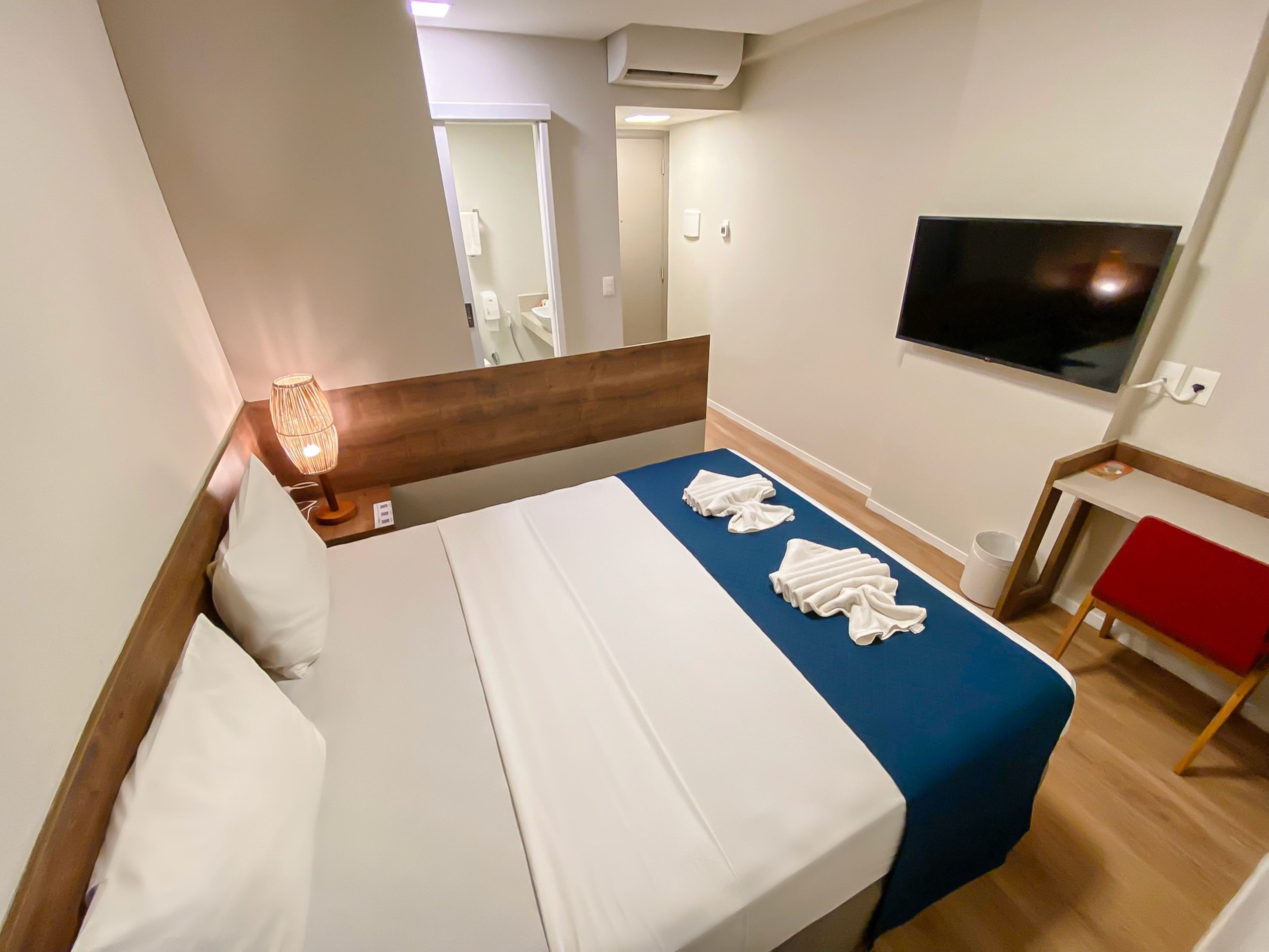 A hotel room with a bed, a TV, a desk, and a chair.