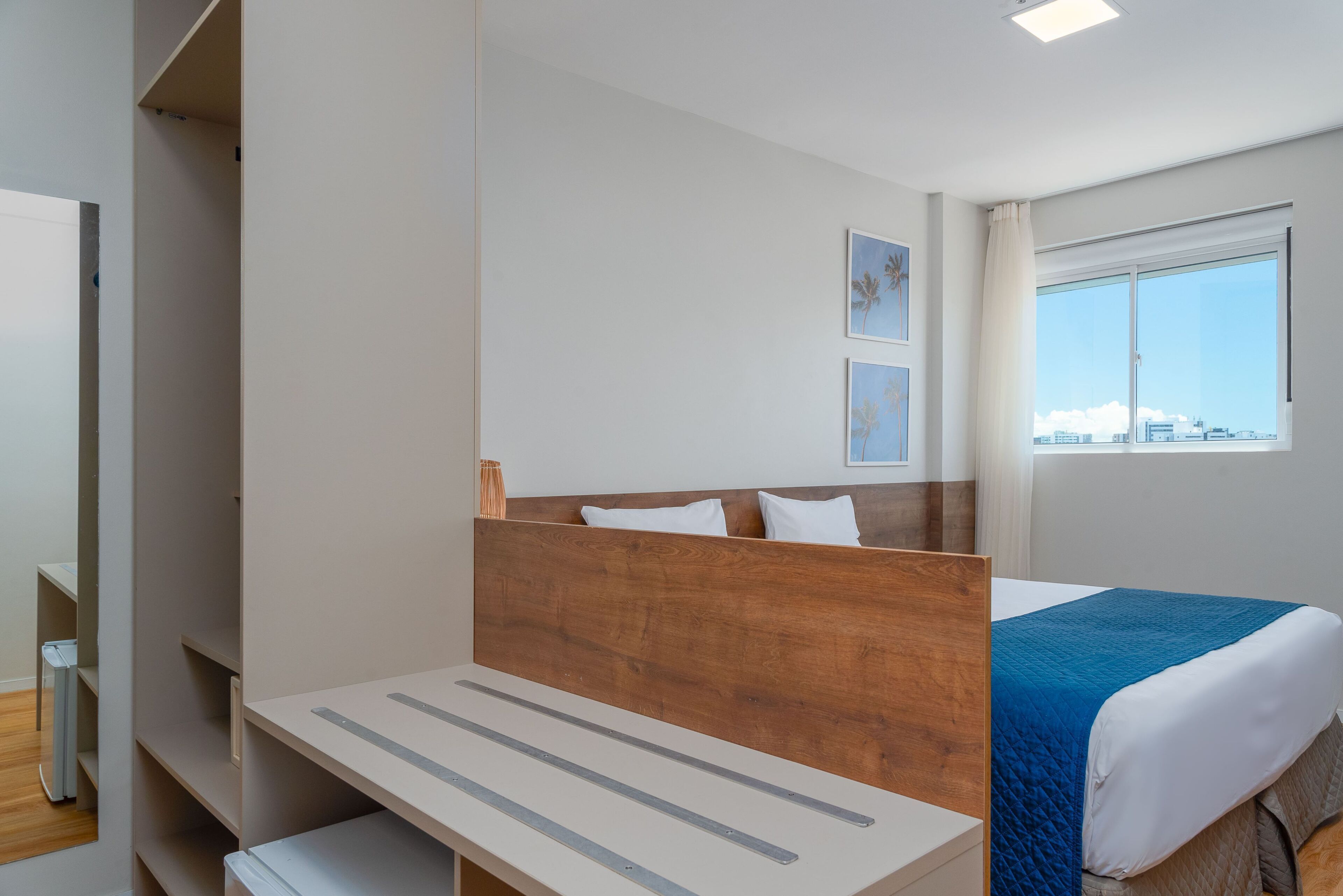 A hotel room with a bed, a bedside table, a wardrobe, and a window with a city view.