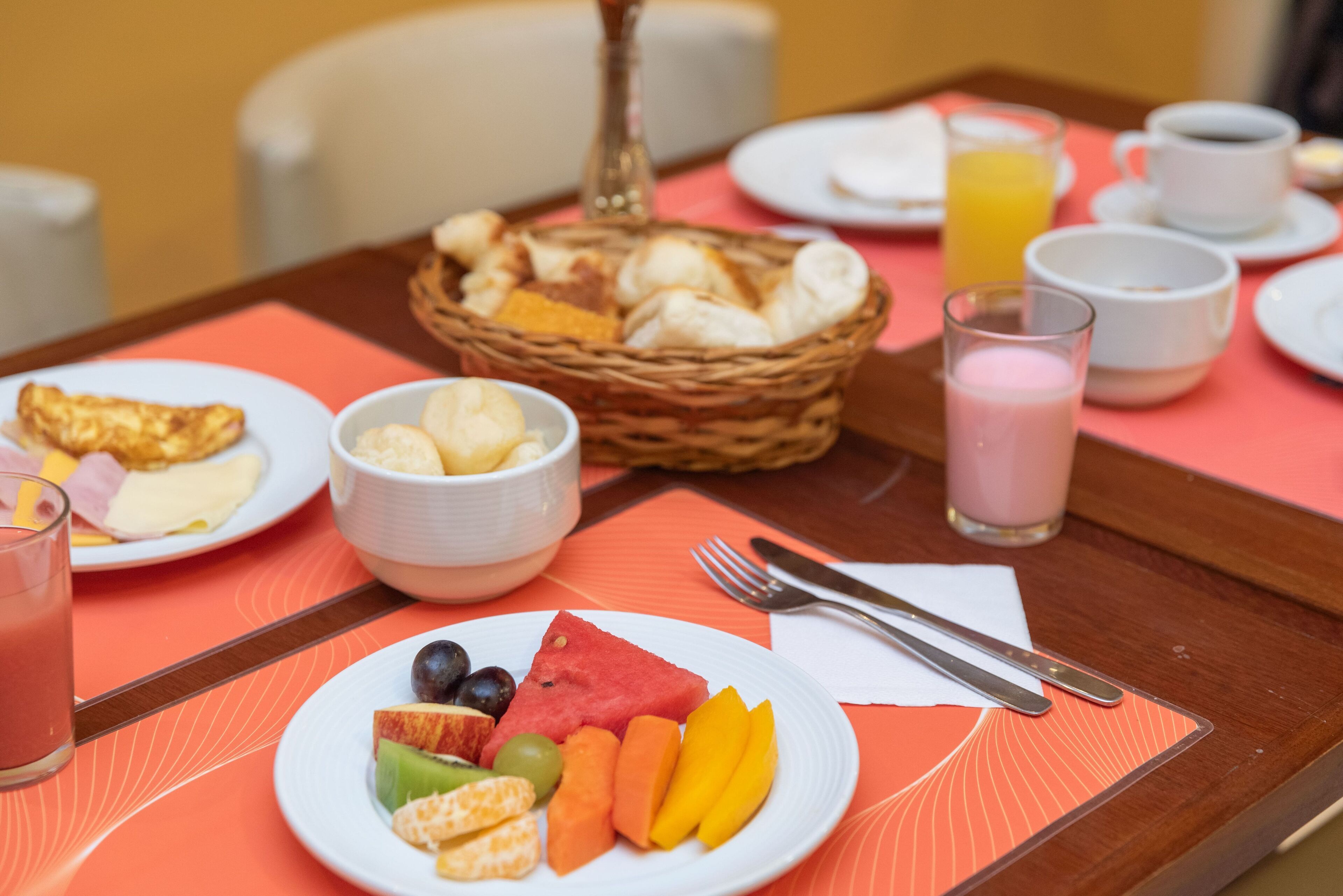 Ein Esstisch mit Fruchtschalen, Brot und einem Glas Saft.