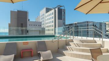 A rooftop pool area with lounge chairs and a glass balustrade.