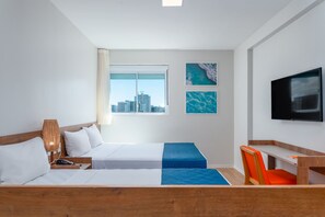 Hotelkamer met een bed, een bureau, een stoel, een televisie en een raam met uitzicht op de stad.