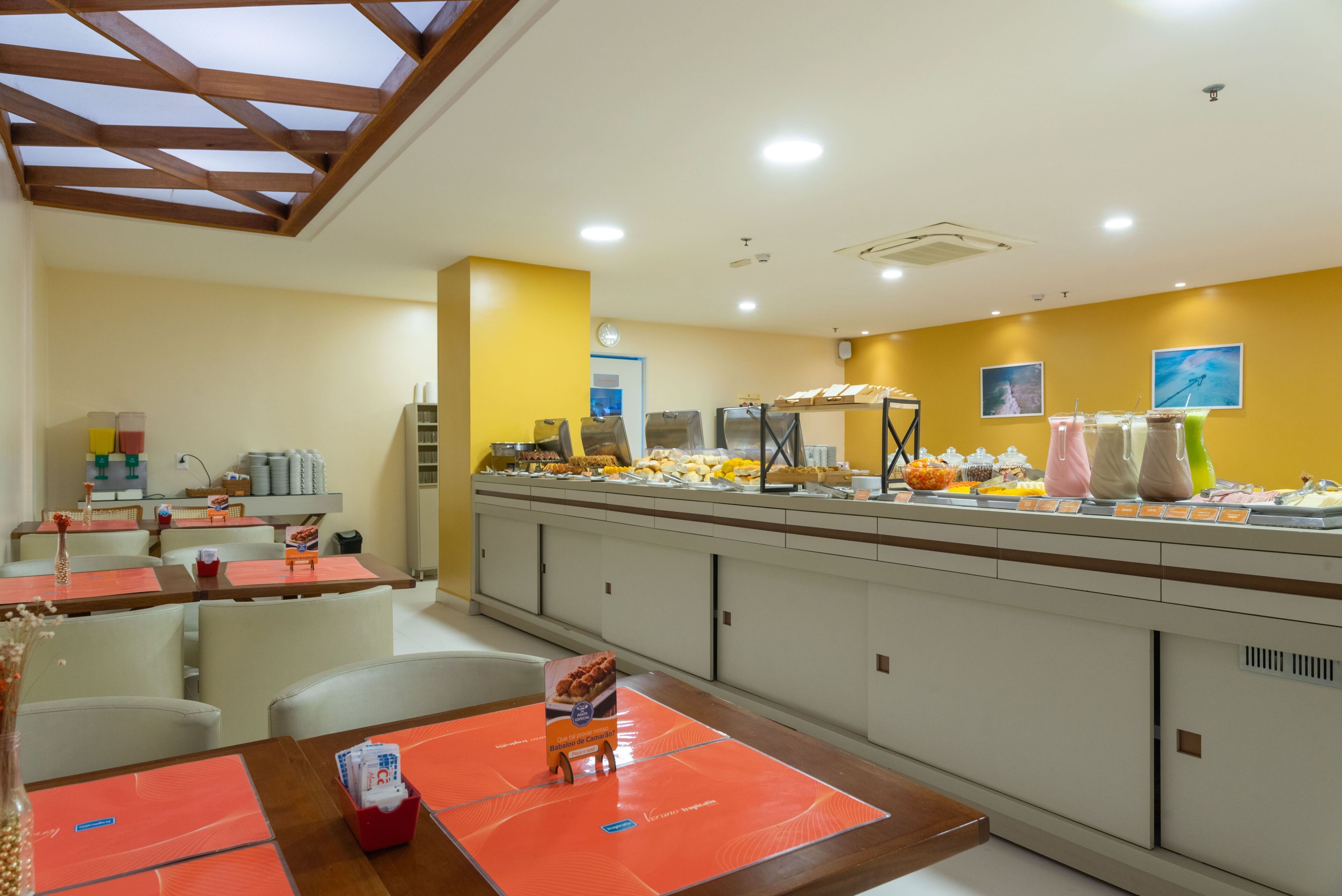 A buffet area with a variety of food options, including fruits, pastries, and beverages. There are multiple seating areas with tables and chairs.