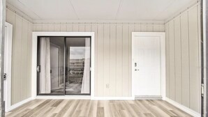 Een kamer met een houten vloer, een schuifglazen deur en een gesloten witte deur.