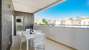 Un balcone con un tavolo apparecchiato per mangiare, una bottiglia di vino e vista su edifici in lontananza.