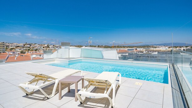 Una piscina sul tetto con acqua cristallina, circondata da poltrone da sdraio bianche e una ringhiera in vetro.