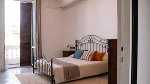 Une chambre à coucher avec un lit, une table de chevet, un vase de fleurs et une vue sur l’extérieur.