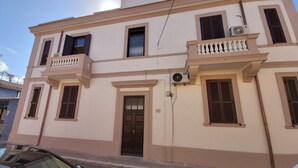 Un immeuble de deux étages doté d’un balcon au deuxième étage, d’une porte avec une plaque numérotée et d’un appareil de climatisation fixé au mur extérieur.