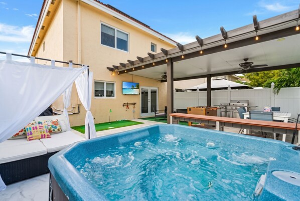 A backyard with a hot tub, a covered patio area, and a pool table.