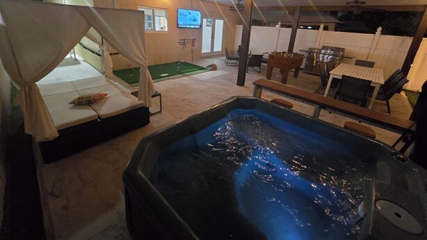 A hot tub and outdoor seating area with a canopy, a foosball table, and a TV screen.
