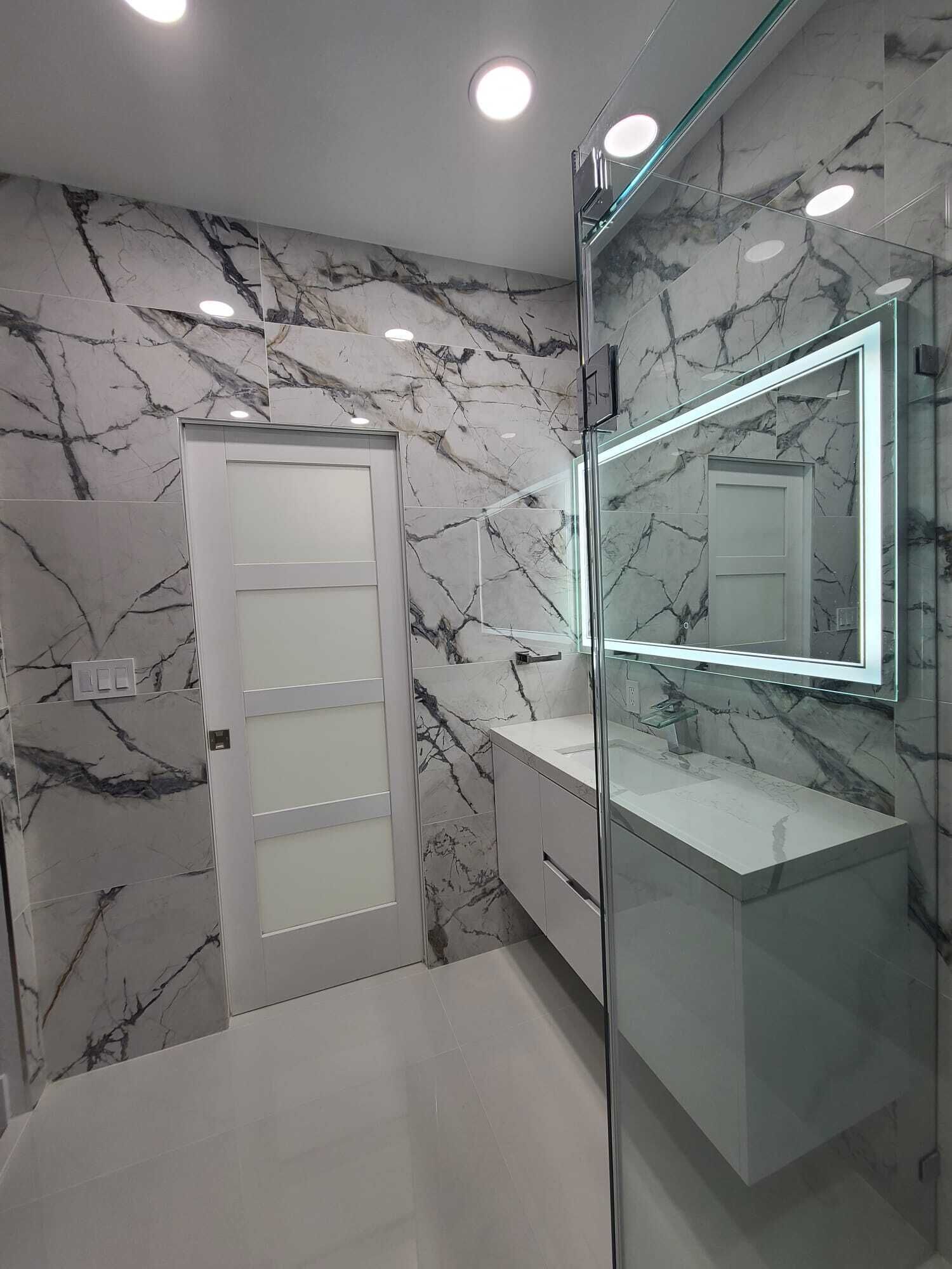 Un bagno moderno con pareti in marmo, box doccia in vetro e un ampio specchio.