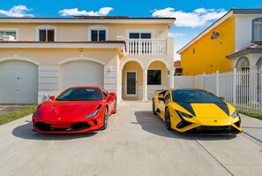 Two luxury sports cars parked in front of a residential building with a white fence and a clear sky.