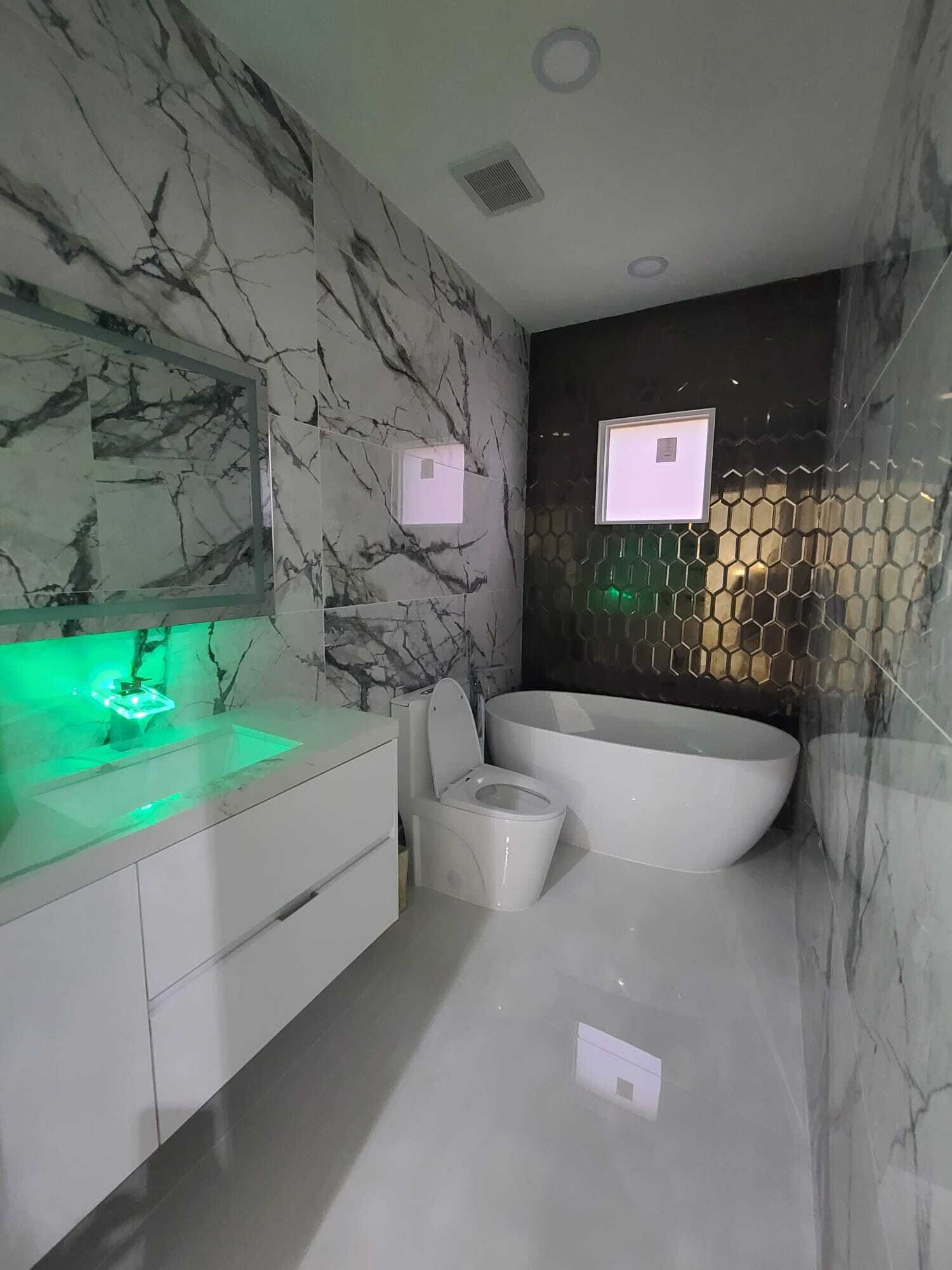 Un bagno moderno con una parete in marmo, una vasca freestanding e un mobile lavabo con un lavandino illuminato di verde.