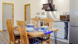 A dining area with a wooden table set for four, a kitchen with modern appliances, and a visible door leading to another room.