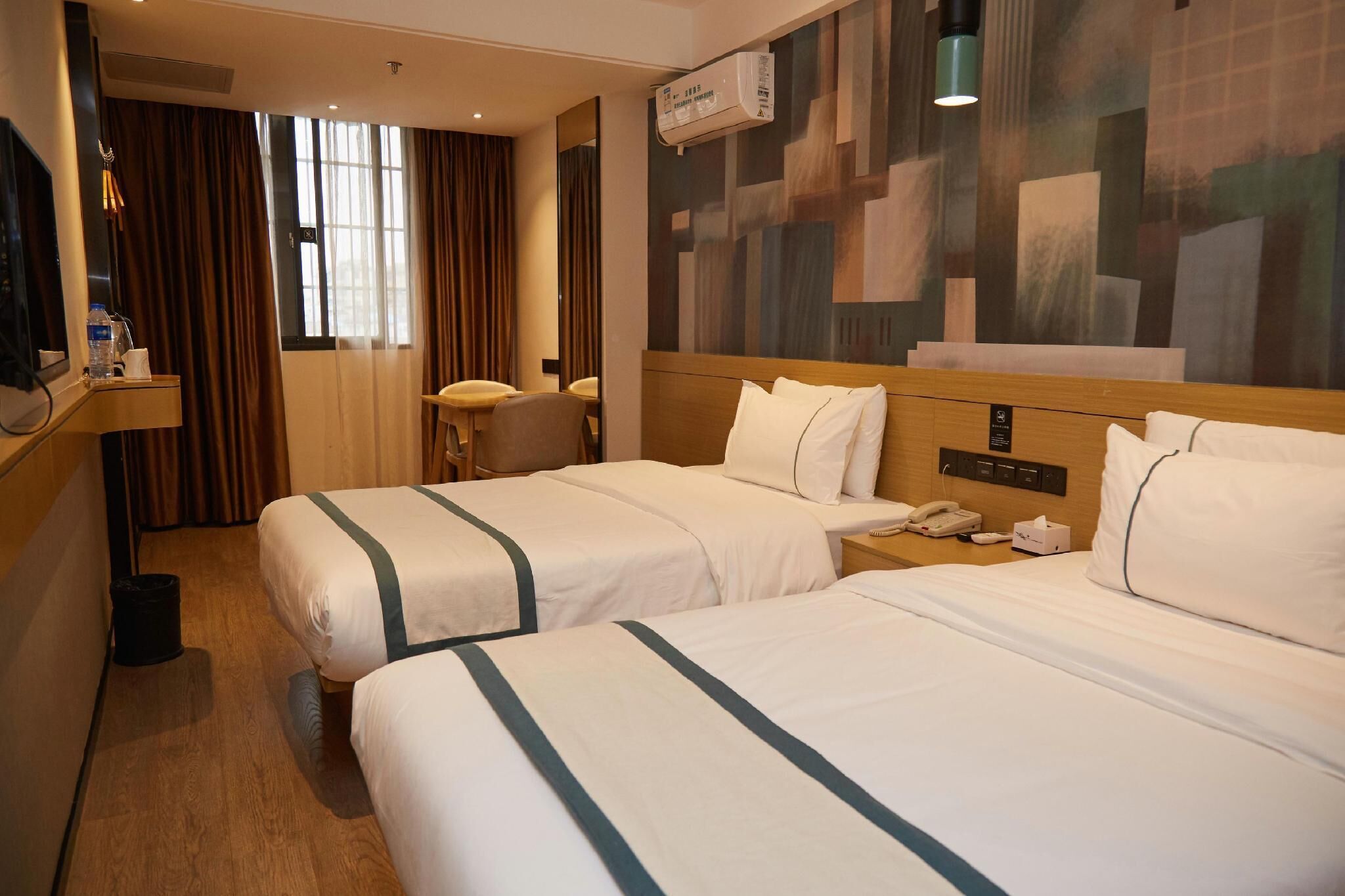 A hotel room with two beds, a desk, a chair, a telephone, and an air conditioning unit.