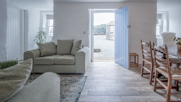 Ein Wohnzimmer mit einer Couch, einem Esstisch mit Stühlen und Blick durch eine geöffnete Tür.