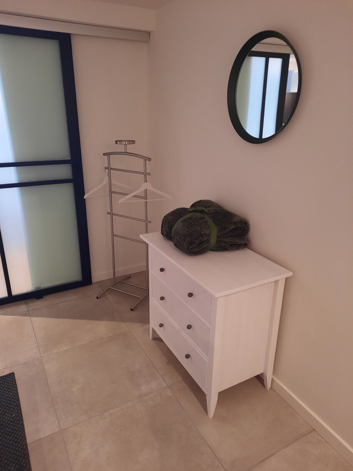 Een kamer met een witte dressoir, een spiegel aan de muur en een kledingrek.