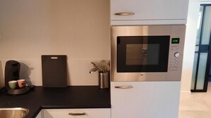 A modern kitchen with a built-in microwave, a coffee maker, and a cutting board. - Souterrain "Edelweiss" (Noordwijk)