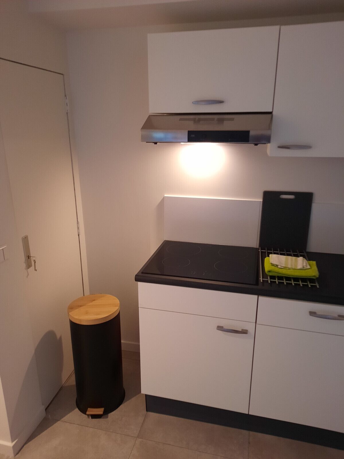 Een kleine keuken met witte kasten, een zwart aanrecht en een rvs-afzuigkap.