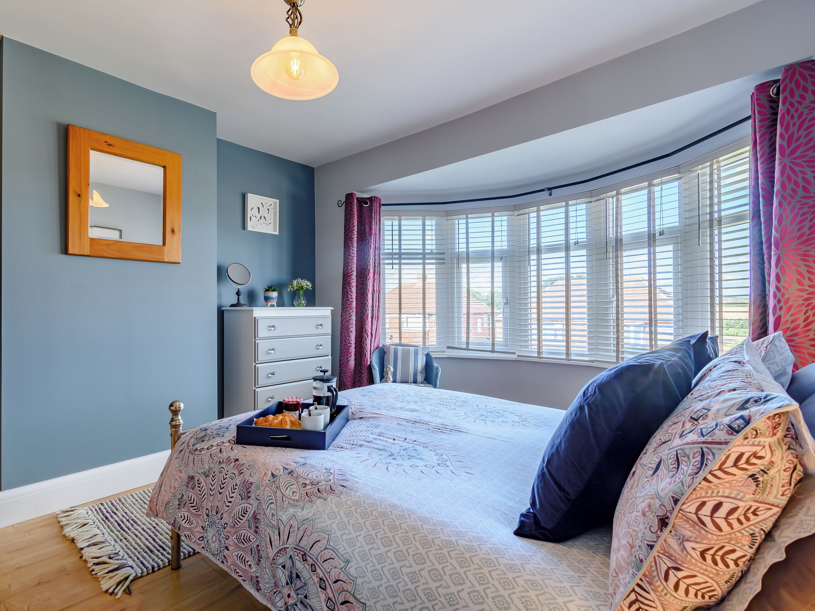 A bedroom with a bed, a dresser, a mirror, and a window with curtains.