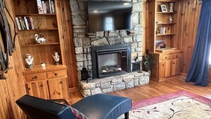 A cozy living room with a stone fireplace, wooden shelves, and a blue sofa.