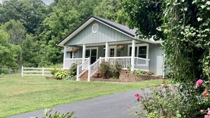 A light blue building with a porch, surrounded by greenery and a white fence.