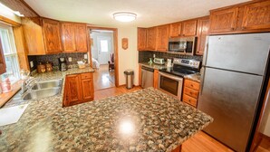 A kitchen with wooden cabinets, granite countertops, stainless steel appliances, and a visible trash can.