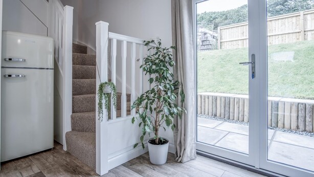 A modern kitchen with a built-in refrigerator, a staircase with a white railing, and a potted plant near a sliding glass door leading to a backyard. - Brook Cottage - 2 Bedroom Cottage - Dale (Haverfordwest)