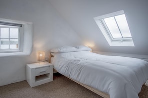 A bedroom with a bed, a bedside table, a lamp, and a skylight.