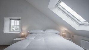 A bedroom with a sloped ceiling, a skylight, a bed with white bedding, two bedside lamps, and a window. - Brook Cottage - 1 Bedroom Cottage - Dale (Haverfordwest)