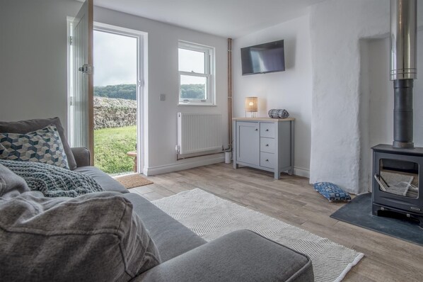 A cozy living room with a sofa, a small cabinet, a TV, and a wood-burning stove.