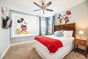 Habitación de hotel con un gran mural de Mickey Mouse, una cama con una colcha roja, un cabecero de madera y un ventilador de techo.