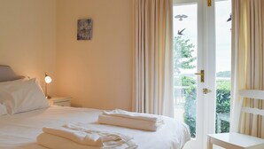 A hotel room with a bed, a nightstand with a lamp, a chair, and a balcony door with curtains. - 2 bedroom accommodation in Clopton, near Kettering (Clopton, near Kettering)