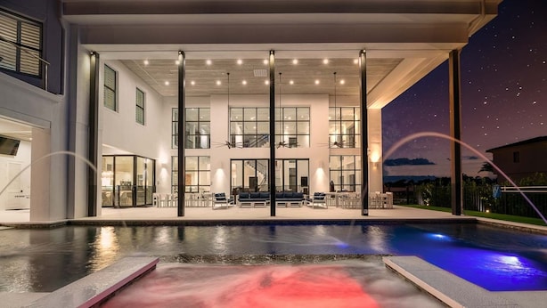 A modern house with a large pool, outdoor seating, and a staircase leading to the upper level.