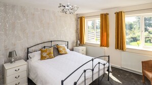 A bedroom with a bed, bedside tables, a lamp, a radiator, and a window with curtains.