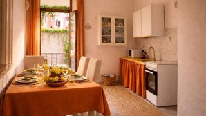 A dining area with a table set for two, a kitchen with a stove and sink, and a window with curtains. - CIVITAVECCHIA SWEET HOME (Civitavecchia)