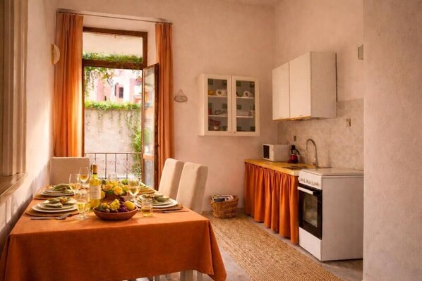A dining area with a table set for two, a kitchen with a stove and sink, and a window with curtains.
