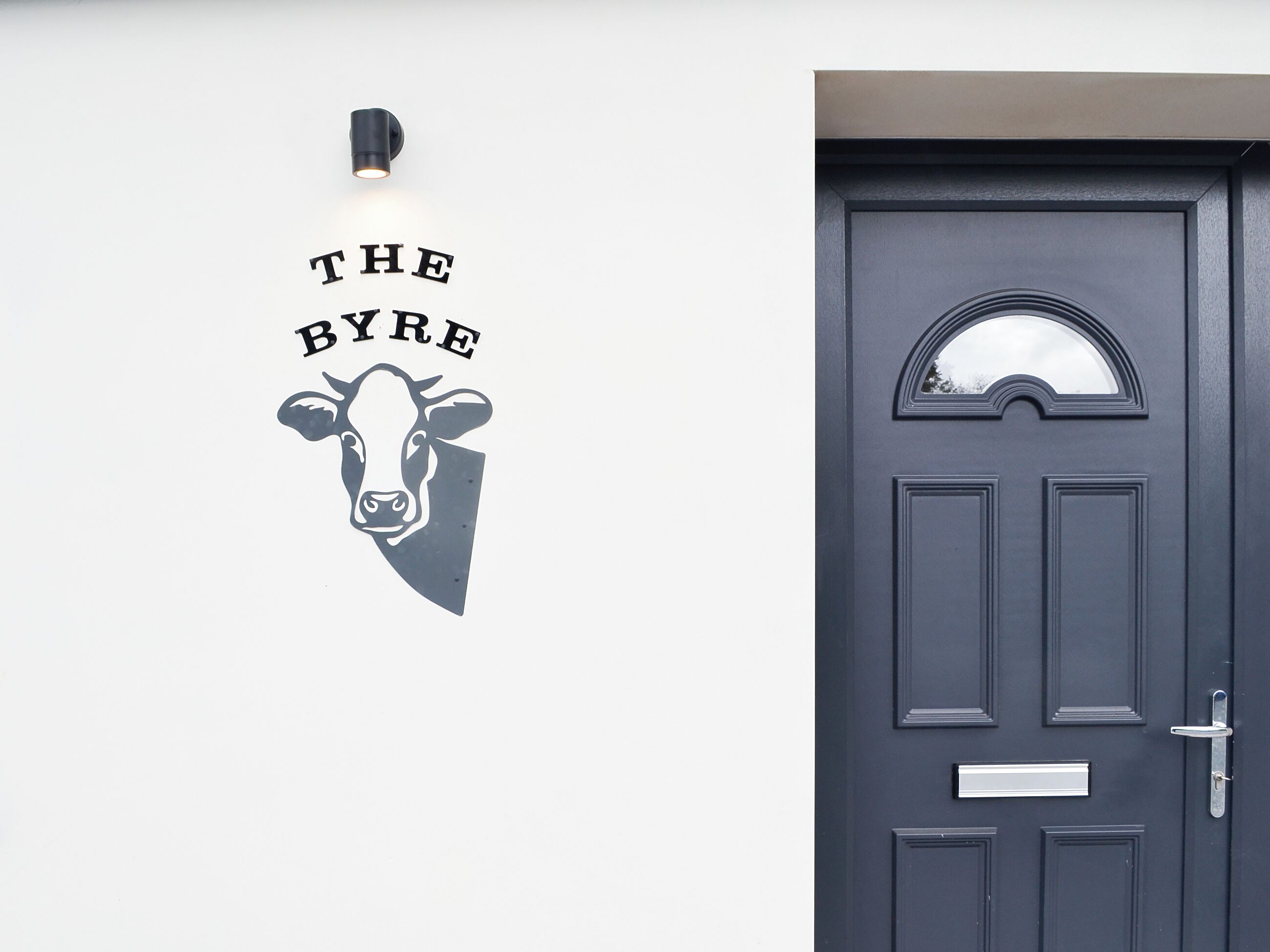 A dark door with a small window above it and a wall-mounted light fixture with a cow's head and the text 'THE BYRE' above it.