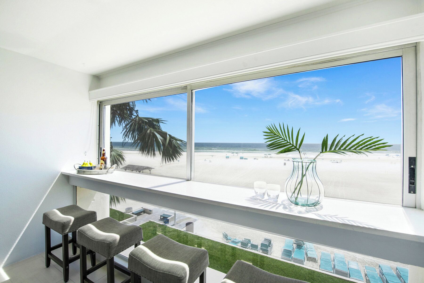 Een balkon met uitzicht op het strand, een glazen vaas met een plant en barstoelen.