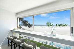 A balcony with a view of the beach, a glass vase with a plant, and bar stools.