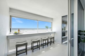 A balcony with a view of the beach, a bar area with stools, and a bottle on the windowsill. - Beautiful fully renovated two bedroom two bathroom condo is located on the third floor (Sarasota)
