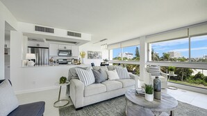 Una sala de estar moderna con un sofá gris, una mesa de centro y vistas de la ciudad a través de amplios ventanales.