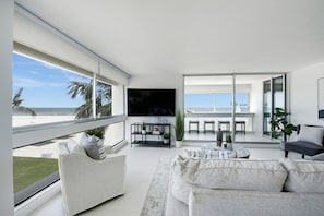 A modern living room with a large TV, a sofa, and a balcony with a view of the beach. - Beautiful fully renovated two bedroom two bathroom condo is located on the third floor (Sarasota)