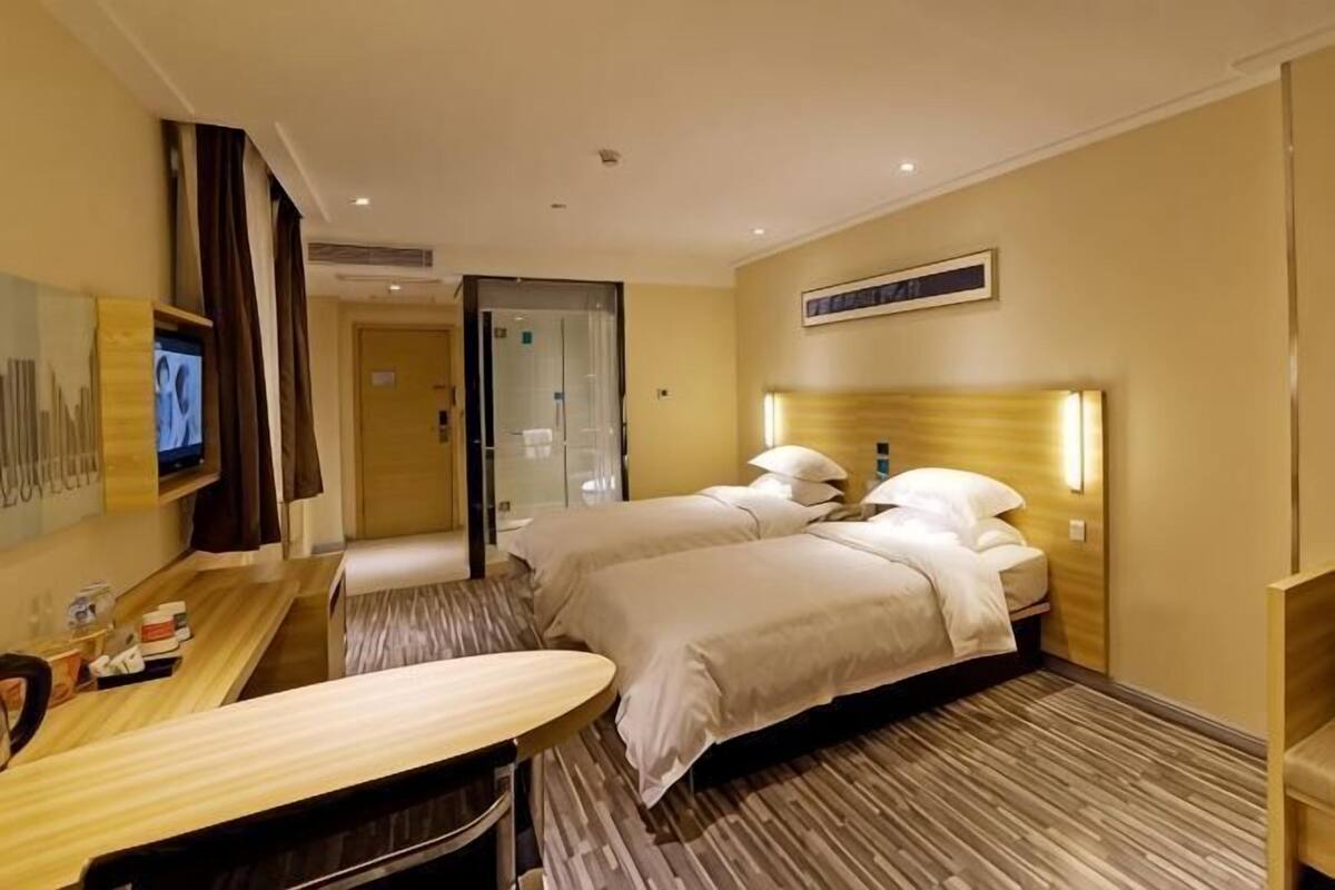 A hotel room with two beds, a desk, a TV, and a bathroom.