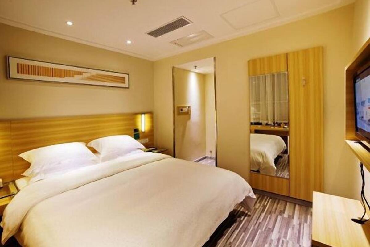 A hotel room with a large bed, a wooden headboard, a flat-screen TV, and a mirror.