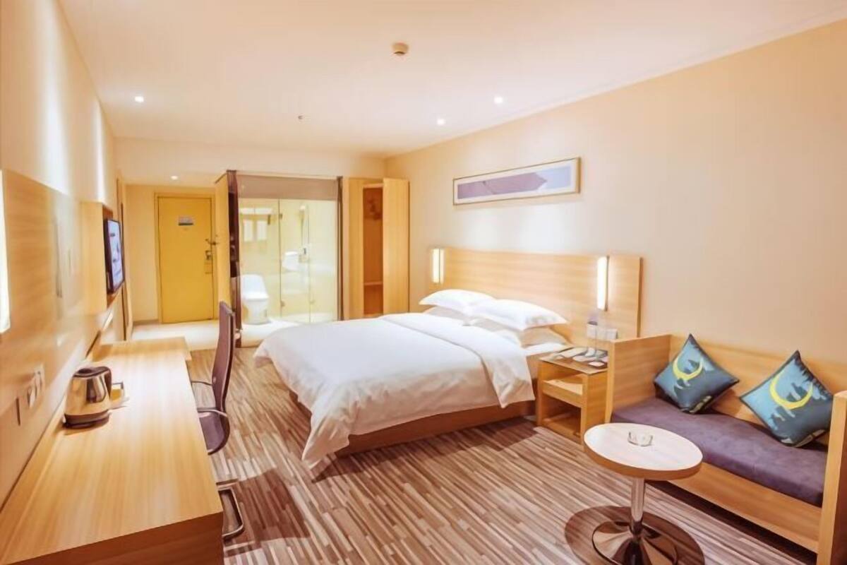 A hotel room with a bed, bedside table, lamp, seating area, and a small round table.
