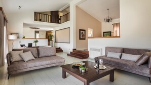 A spacious living room with a brown sofa, a coffee table with decorative items, and a staircase leading to an upper level. - Malibu Superior Villa (Kefalonia)