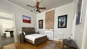A bedroom with a wooden bed, a ceiling fan, a brick wall, and a small table with a decorative item. - Historic Gem w/ Jacuzzi / Prime Streetcar Spot (New Orleans)