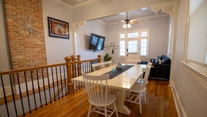 A dining area with a wooden table, white chairs, and a brick wall. - Historic Gem w/ Jacuzzi / Prime Streetcar Spot (New Orleans)